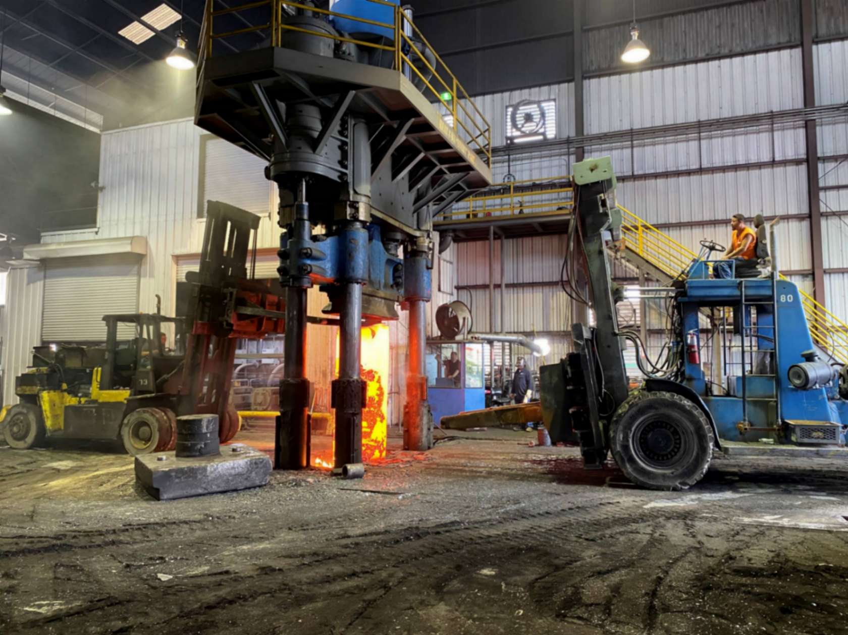 A multi-ram hydraulic press with FCI branding and a glowing workpiece in the die