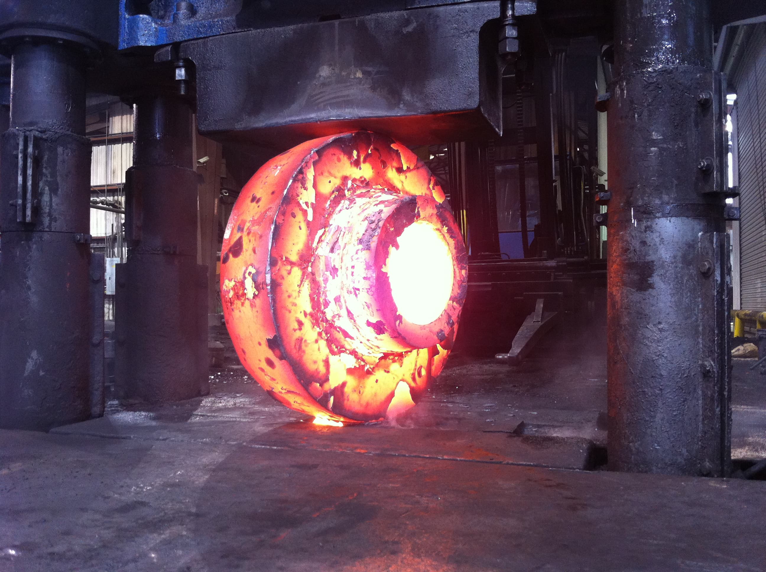 A glowing ring forging held between the columns of an FCI hydraulic press