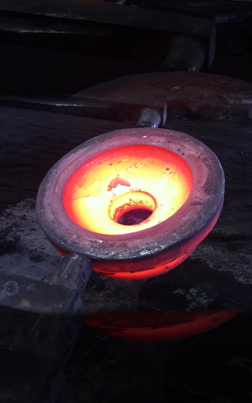 A glowing ring forging standing on a press anvil in a dark shop