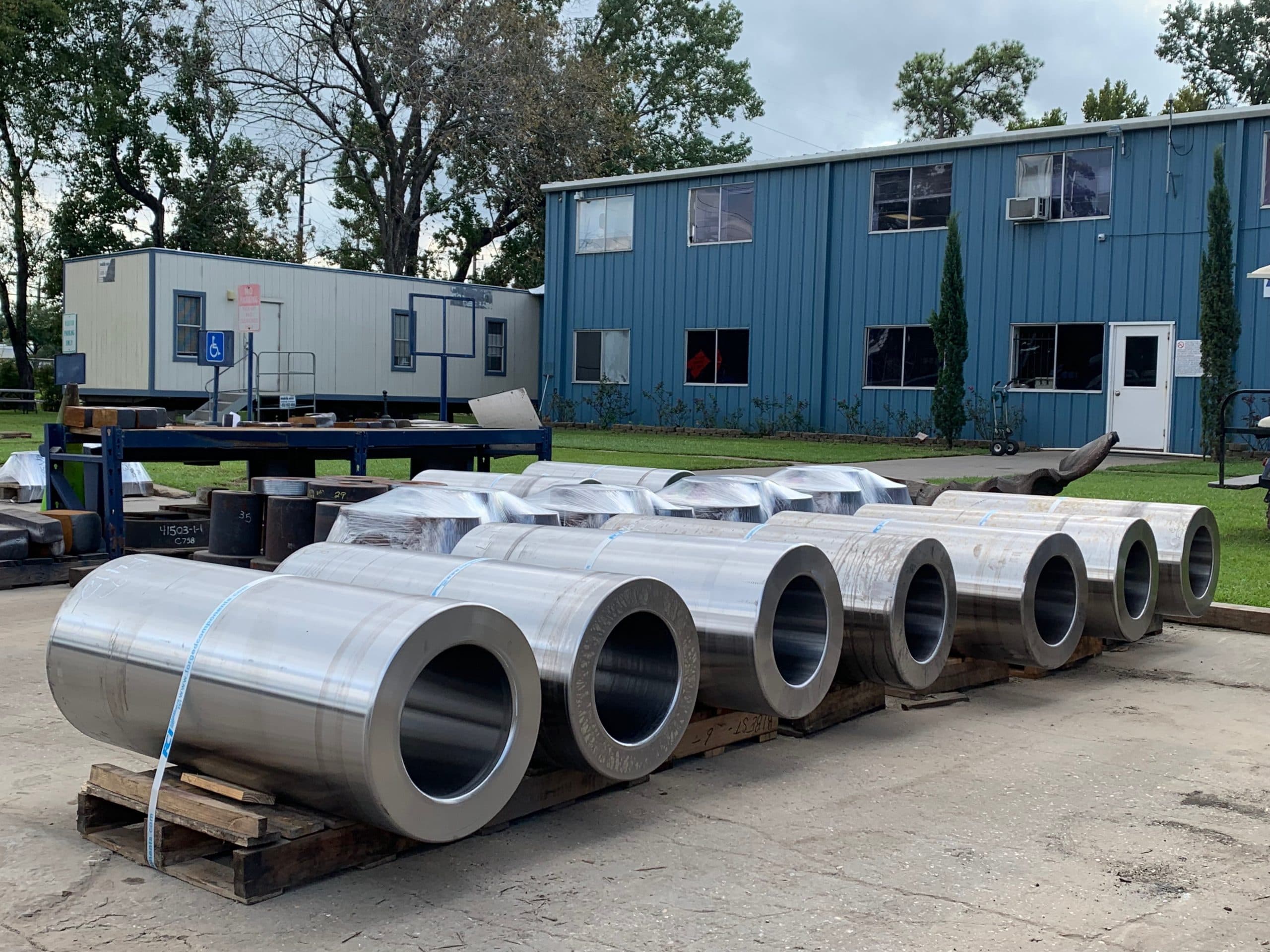 A row of rough-machined heavy-wall cylinders in front of blue shop buildings
